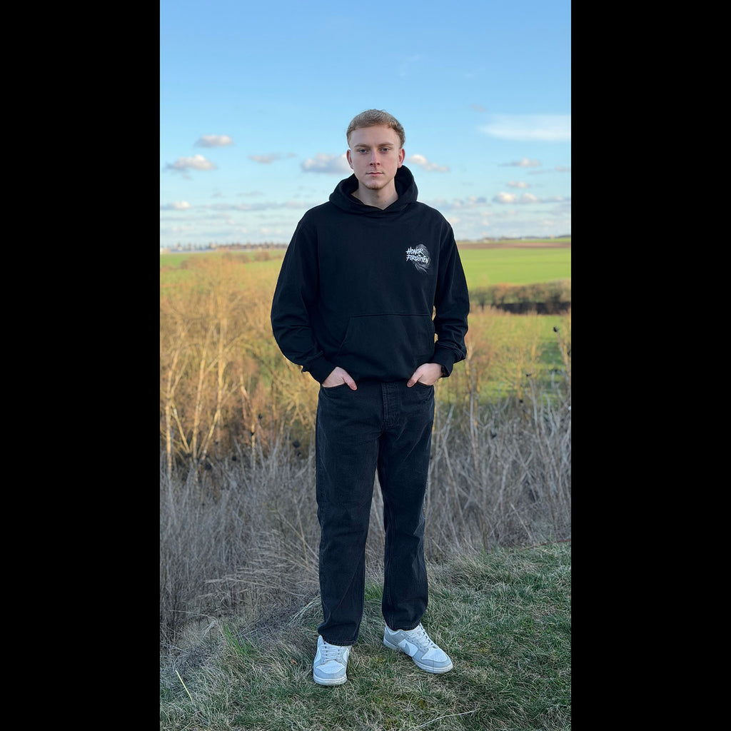 Schwarzer Honor Forgotten Hoodie am Model im Outdoor-Fotoshooting, Frontansicht mit Brustlogo.