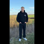 Schwarzer Honor Forgotten Hoodie am Model im Outdoor-Fotoshooting, Frontansicht mit Brustlogo.